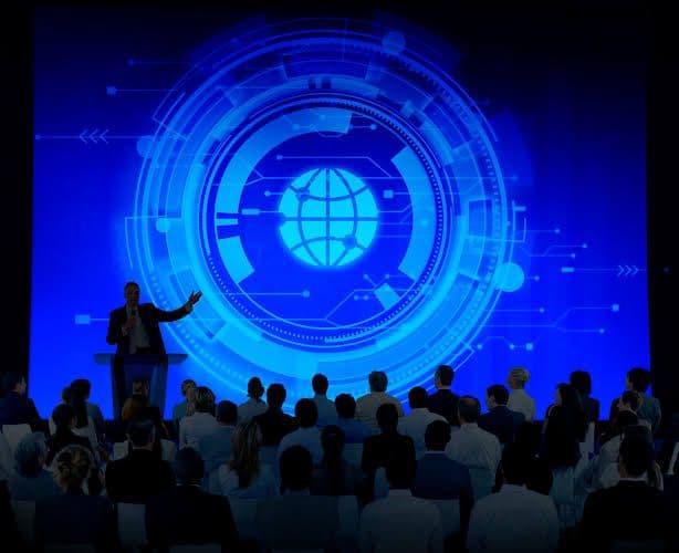 A conference speaker addressing a seated audience in front of a large digital globe display
