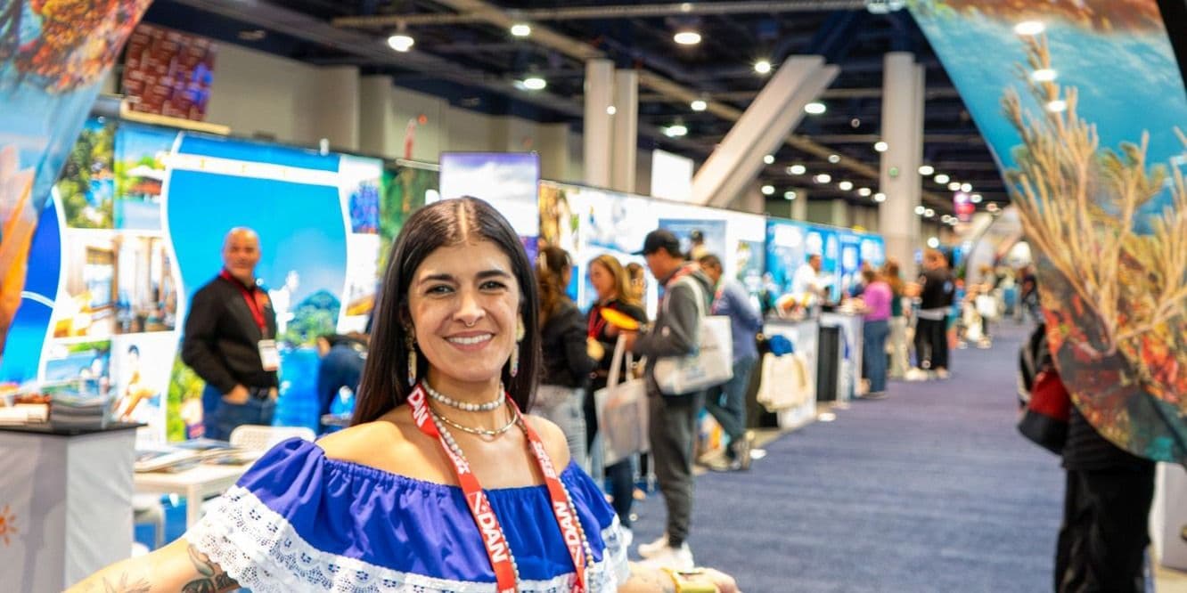 DEMA Show 2024 attendee in the exhibit hall with destination booths behind her
