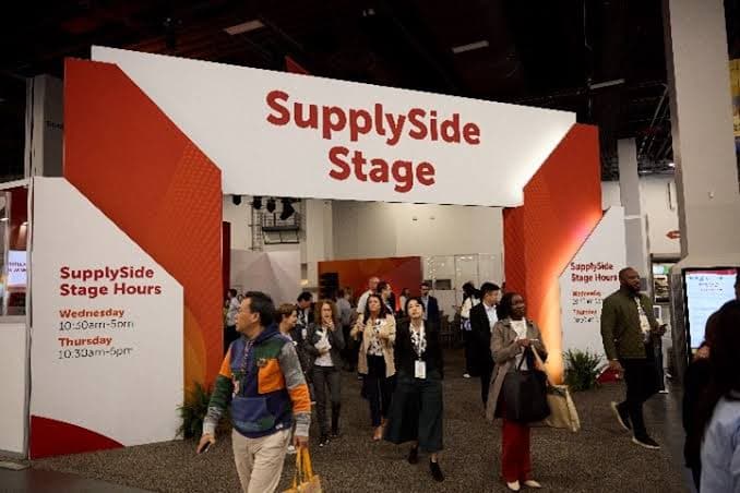 Attendees walking past the SupplySide Stage entrance archway with posted session hours