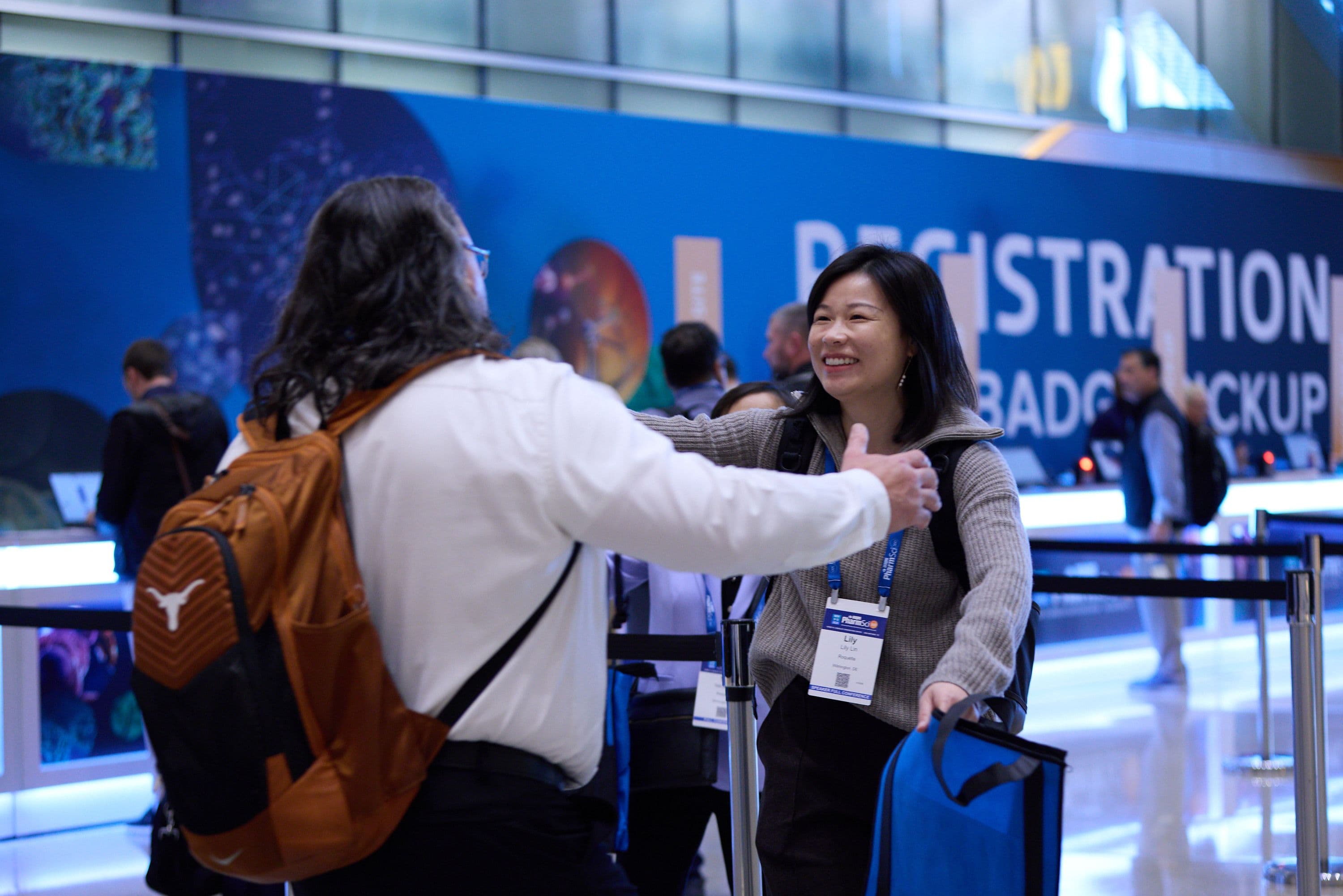 Two PharmSci 360 attendees greeting each other beside the event registration desk