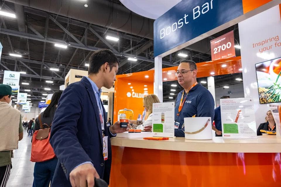 An attendee sampling a product while speaking with an exhibitor at the Caldic Boost Bar booth