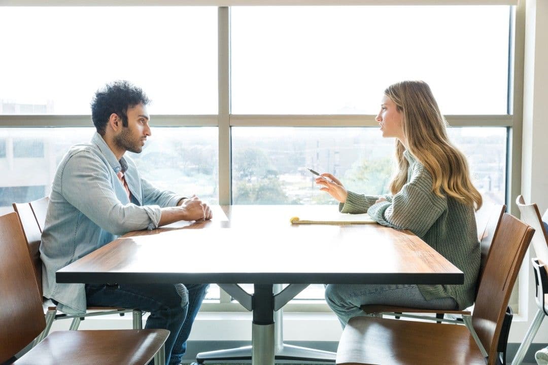 Two attendees seated across a table in a bright, window-lit room during a one-on-one meeting at the event