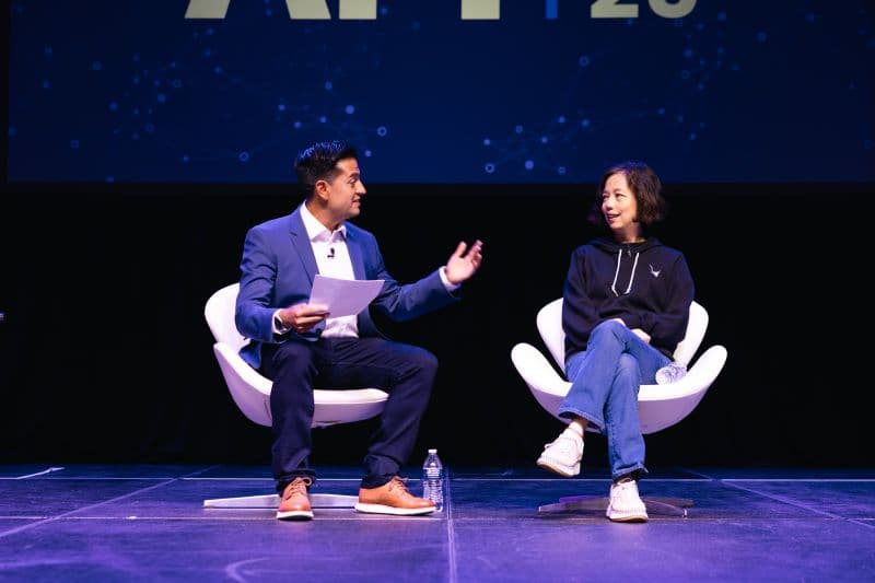 Host and guest speaker seated in white chairs during a fireside chat session on the AI4 2026 main stage